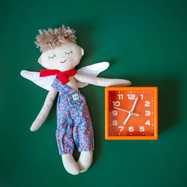 Sleeping angel toy and orange alarm clock on a dark green background.