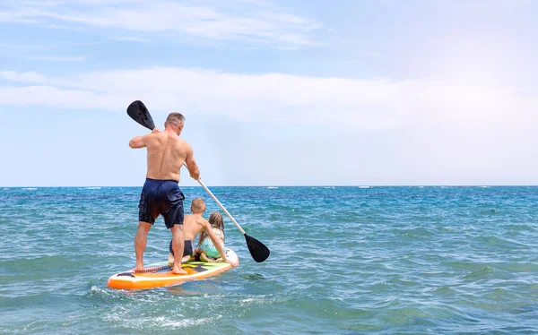 Ein Vater und zwei Kinder fahren mit einem Sup Board auf dem Meer. Stand up paddle board. — Stockfoto