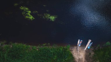 Nehrin ya da gölün karanlık sularında kıyıya demirlemiş iki tekne var.