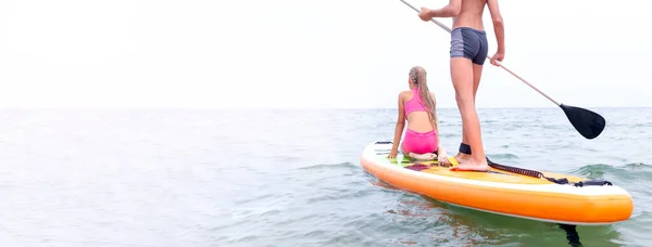 Twee personen op het peddelbord op het kalme zeeoppervlak bewegen naar de horizon. — Stockfoto