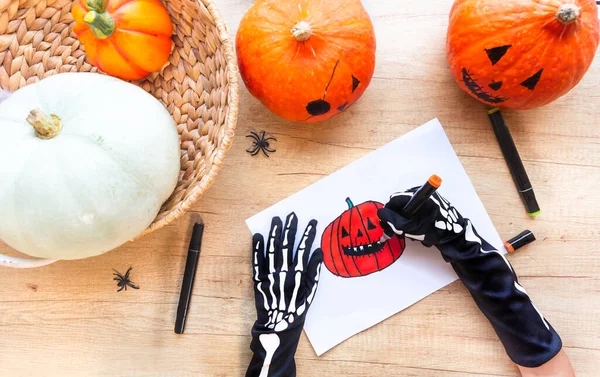 Hands in gloves with bones are drawing a sketch with markers a laughing pumpkin — Stock Photo, Image