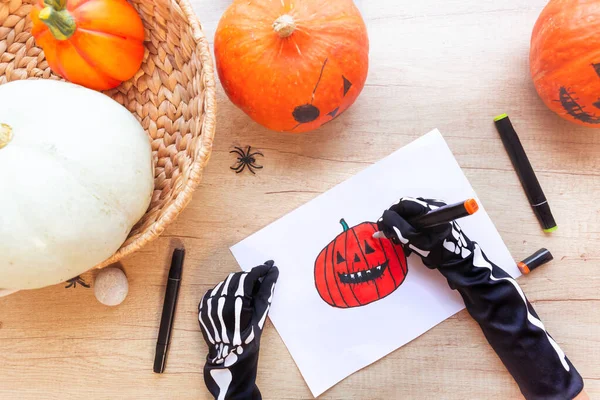 Hands in black gloves are drawing a laughing pumpkin, on a desk. Halloween. — Stock Photo, Image