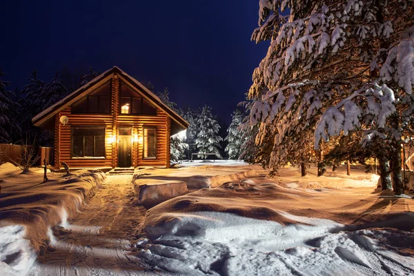 Un sentiero tra i cumuli di neve che conduce ad una rustica casa di tronchi, una notte d'inverno. — Foto Stock