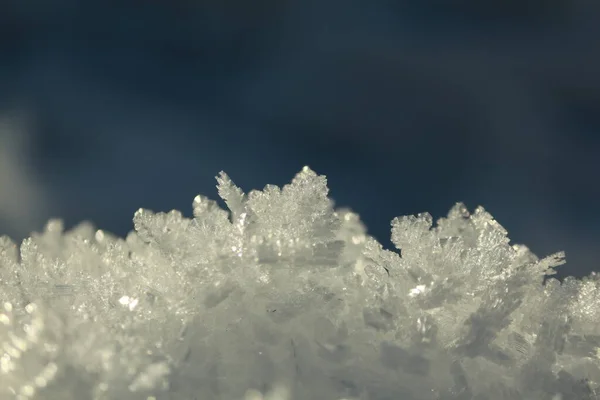 Abstract snow crystals pattern. A surface of crystallized frost sparkles in the sun against a blue sky on a winter day. Winter natural background of snow ice crystals against a blue clear sky.