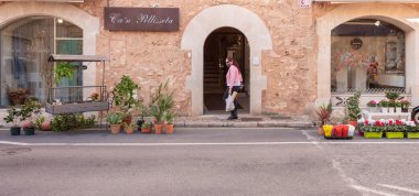 Campos, Balear Adaları / İspanya; Ekim 2020: Çiçekçi dükkanının önü, sokakta çiçekler. Alışveriş çantalı ve maskeli bir kadın. Yeni normal kavram