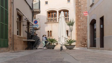 Campos, Balear Adaları / İspanya; Kasım 2020: Campos kentinde kapalı bir kafeterya terası olan ticari cadde. Sandalyeler ve masalar zincirle bağlanmış. Arka planda iki kadın var.