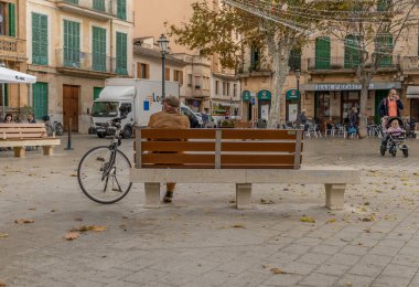Llucmajor, İspanya: 17 Aralık 2020: Llucmajor 'ın ana meydanında bisiklet maskesiyle halka açık bir bankta oturan yaşlı kişi. Yeni normal