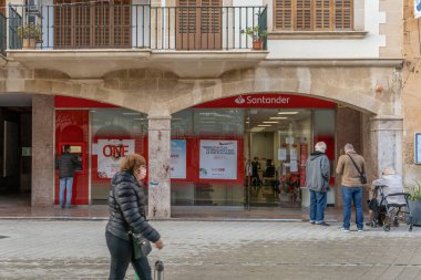Llucmajor, İspanya; 17 Aralık 2020: Coronavirus 'un aldığı önlemler nedeniyle dışarıda bekleyen yüz maskesi takan müşterileri olan bir İspanyol bankasının cephesi. - Yeni normal