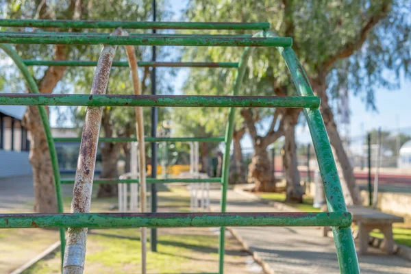 Close-up of a green vintage metal swing, with the background out of focus, located in a park on a sunny day