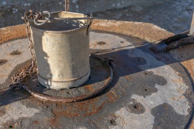 Güneşli bir günde metal kapaklı eski bir taşın üzerindeki metal kova.
