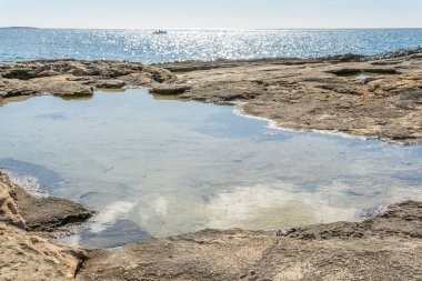 Durgun deniz suyuyla Mallorca adasının kayalık kıyıları. Arka planda odak dışı Akdeniz ve güneşli bir günde yelken açan bir yat.