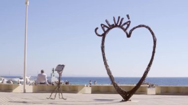 Palmanova, İspanya; 20 Şubat 2021: Palmanova 'nın Majorcan turistik bölgesinde demir kalpli bir heykel ile deniz gezintisi. Yüz maskesiyle yürüyen yayalar. Yeni normal kavram