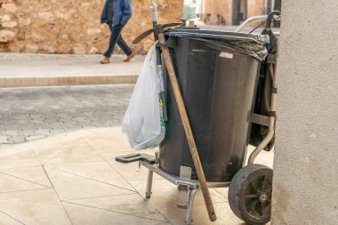 Sokak süpürücünün arabası. Şafak vakti bir şehir sokağında süpürge ve kovayla. Arka planda tanınmayan yayalar