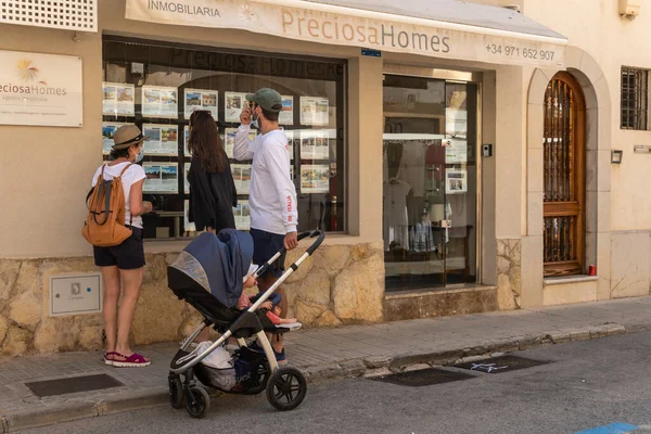 Campos, İspanya; 12 Haziran 2021: Majorcan kasabası Campos 'taki bir emlak acentesinin camından bakan yüzü maskeli Avrupalı turist ailesi. Yeni normallik kavramı