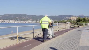 Palma de Mallorca, İspanya; 25 Haziran 2021: Güneşli bir sabah Palma de Mallorca şehrinde sokak temizleyicisi kovası ve fırçasıyla yürüyor