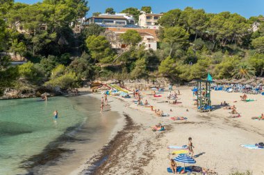 Cala Santanyi, İspanya; 11 Eylül 2021: Mallorca adasındaki Cala Santanyi plajının genel manzarası, kumsalda ve güneşli bir sabahta Akdeniz 'de banyo yapanlar