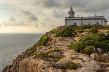 Mallorca adasının kayalık sahilindeki Kaptan Blanc deniz feneri. Arka planda Akdeniz 'in deniz manzarası gün batımında bulutlarla birlikte. Muhteşem manzara.