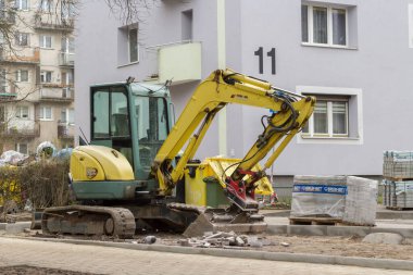Sarı mini kazıcı apartmanın yakınındaki kaldırımda çalışıyor..