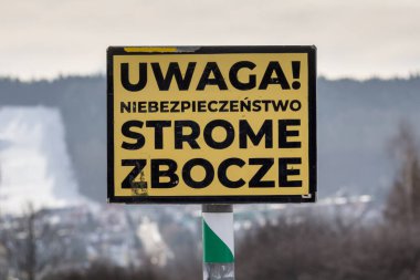 Lehçe uyarı işareti ile metin uwaga tehlikesi bulanık kış manzarasında dik yamaç.