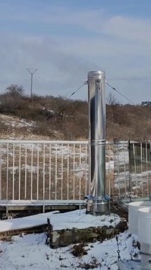 Paslanmaz çelik ısıtma borusu görünür bir buharla dışarıda, karlı yamaçta, bulutlu kış gökyüzünün altında çitlerin yanında yükseliyor..