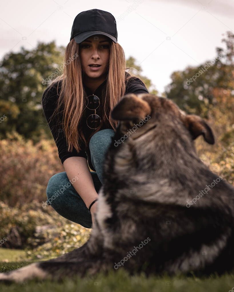 Vertical shot of a woman making a shocked expression as she is trying to pull the stick out of the dogs mouth. Playing a game of fetch and the dog wont let go of his toy