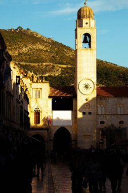 Eski Dubrovnik kasabasındaki ana Stradun caddesinde öğleden sonra günbatımının dikey görüntüsü. Covid mevsiminde sokaklarda çok fazla insan yürümüyor. Acımasız gölgenin altında gizlenmiş yayalar.