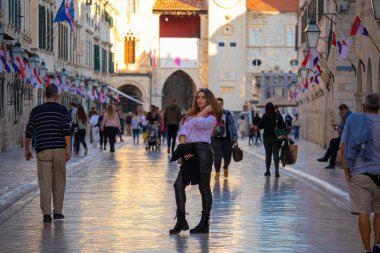 Dubrovnik Hırvatistan Kasım 2020 'de eski Dubrovnik kasabasındaki Stradun Caddesi' nin ortasında duran Brunette, çok sayıda kişinin geçtiği pozunu verdi. Covid mevsiminde sonbaharda yürüyen turistler