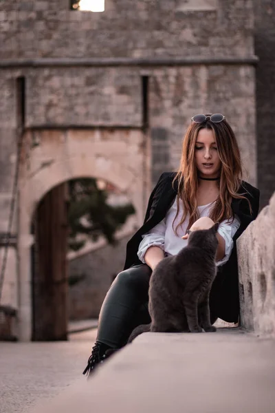 Woman sitting outside with a stray cat that is sitting down next to her. Cat with a serious look does not care about the human next to her.