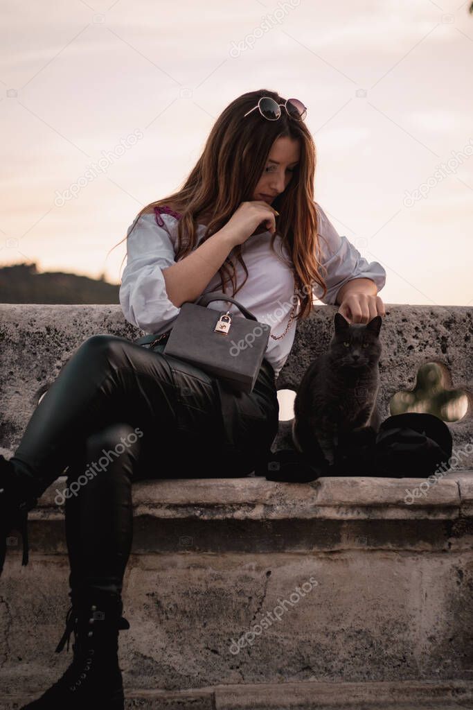 Woman sitting outside with a stray cat that is sitting down next to her. Cat with a serious look does not care about the human next to her.