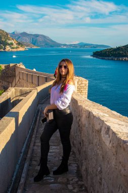 Sıcak bir sonbahar gününde antik şehri keşfeden turist Dubrovnik 'in eski şehir duvarlarında poz veren çekici esmer gezgin. Beyaz gömlek ve siyah deri pantolon giyiyor.