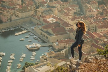 Çekici esmer, Dubrovnik şehrinin üzerinde duran bir kayanın kenarında duruyor. Görkemli antik şehrin üzerinde güzel altın saat, sonbaharda gezginler bölgeyi ziyaret ediyor.
