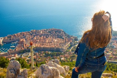 Srd Dağı 'nın tepesinde dikilip uzaktan Dubrovnik şehrini seyreden bir kızın omzunun üstünden. Parlak Adriyatik Denizi ile çevrili antik ünlü şehir