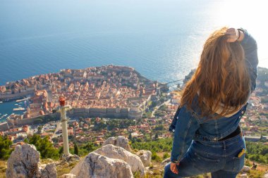 Srd Dağı 'nın tepesinde dikilip uzaktan Dubrovnik şehrini seyreden bir kızın omzunun üstünden. Parlak Adriyatik Denizi ile çevrili antik ünlü şehir
