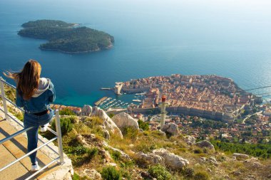 Çekici esmer gezgin Dubrovnik şehrinin yukarısındaki bir korkulukta oturuyor, Srd dağının manzarası. Mavi Adriyatik Denizi ile çevrili tarihi şehre bakıyorum.