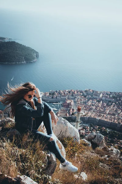 stock image Moody dark vertical portrait of a girl sitting above the city of Dubrovnik on a cold autumn day, wind blowing her hair as she tries to calm it