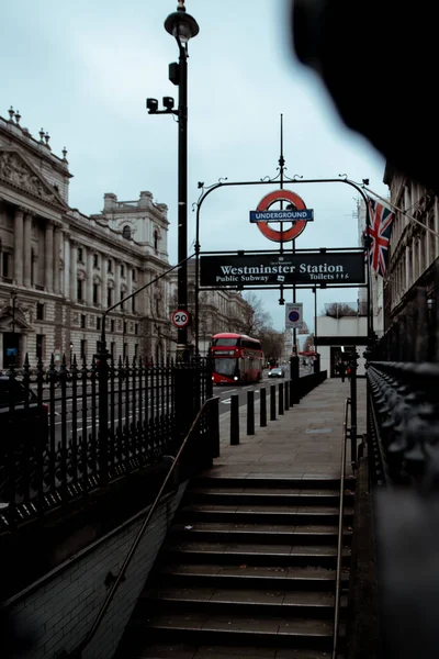 ロンドン英国2021年1月ウェストミンスター地下鉄駅への入り口 寒い冬の日 背景に組合ジャックフラグ 赤のダブルデッキバスは国家のCovidロックダウン中に通過します — ストック写真