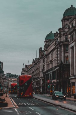 Londra İngiltere Şubat 2021 dikey çekim iki parlak kırmızı çift katlı otobüs, geç saatlerde Londra 'dan geçiyor. Arka plandaki binalardan inanılmaz bir parıltı.