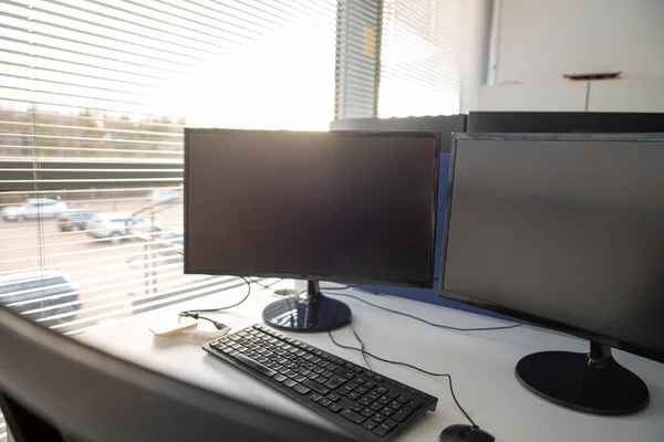 Sandalyeler ve çift monitörler bir ofiste, insanlar covid salgını sırasında evden çalışırken boş. Parlak geniş pencere, güneş ışığının geçmesine izin veriyor. Ofis işleri, yazılım geliştirme kavramları