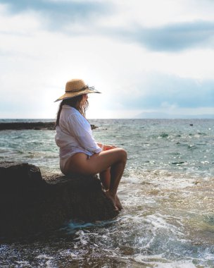 Deniz kenarındaki bir kayanın üzerinde oturan harika bir esmerin yan görüntüsü. 2021 yazında Vis adasında güzel bir deniz mavisi. Dalgalar kıyılara vuruyor