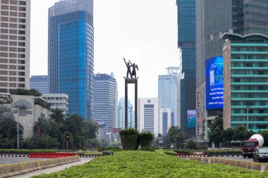 Jakarta / Endonezya - 25 Ekim 2020. Endonezya Oteli 'nin çevresindeki Jakarta' nın karşılama heykeli, gökdelenlerin arka planı ve önünde yeşil bir bahçe bulunuyor..