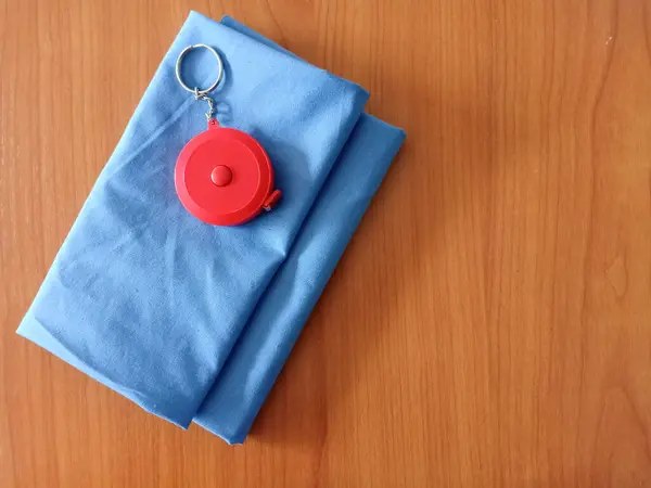 コピースペースのある木製の背景の青い布に赤い丸テープの測定 — ストック写真