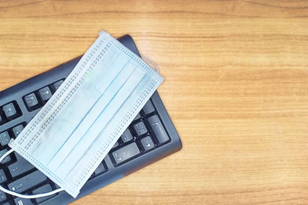 blue face mask on black keyboard with wood texture. New normal concept for workplace.