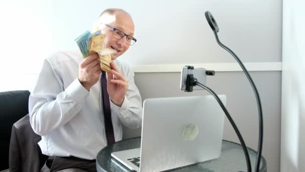 Un uomo caucasico con un fan dei soldi in mano, guadagnati su Internet. Parla tramite collegamento video. — Video Stock