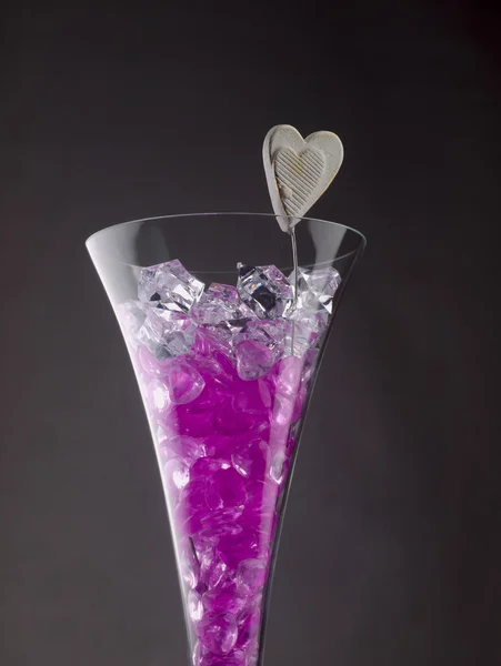 Glass of champagne filled with purple hearts and ice crystals. — Stock Photo, Image