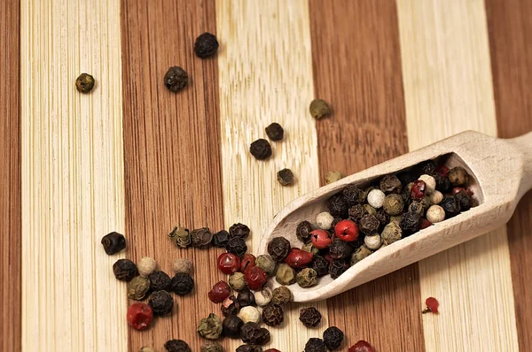 Grains of colored pepper on a wooden plank. — Stock Photo, Image