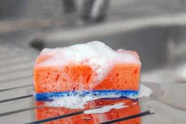 Paslanmaz çelik lavaboda sabunlu turuncu sünger. Bulaşık yıkama ve temizlik aletleri. Bulaşık ve mutfak eşyalarının temizlenmesi için araç.