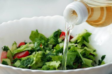 Taze salata kâsesine dökülen sebze yağına yakın plan.
