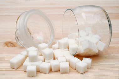 Tahta arka planda devrilmiş cam şeker kasesinden şeker küpleri döküldü.