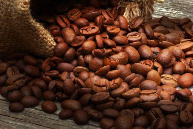 Yakın plan kavrulmuş kahve çekirdekleri ahşap arka planda çuval bezinden döküldü.