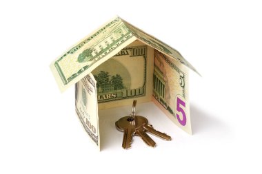 Beyaz arka planda dolar banknotlarından yapılmış bir evin içinde bir sürü anahtar var.